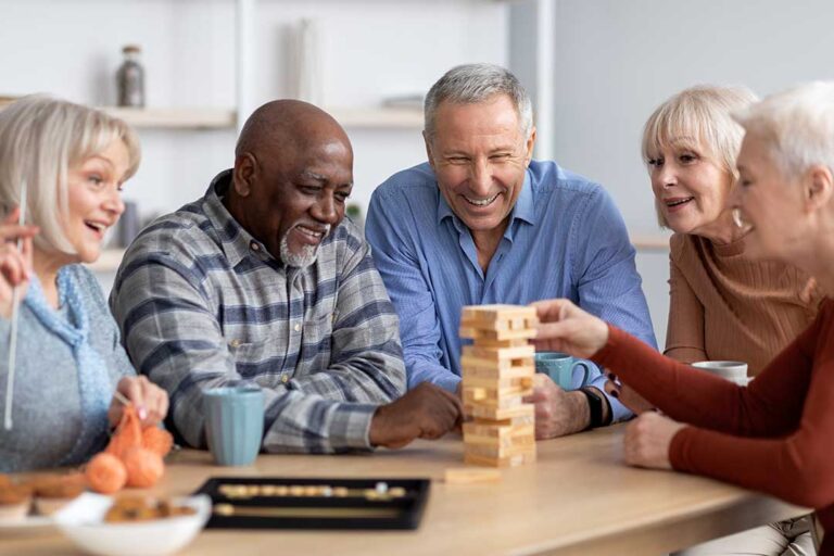 An older adult sitting comfortably in a well-lit room, chatting with a visitor and surrounded by personal mementos.